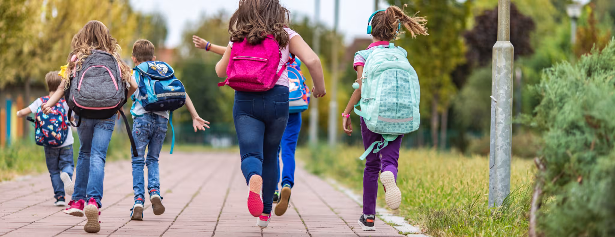 School children wearing backpacks running with their backs turned to the camera.