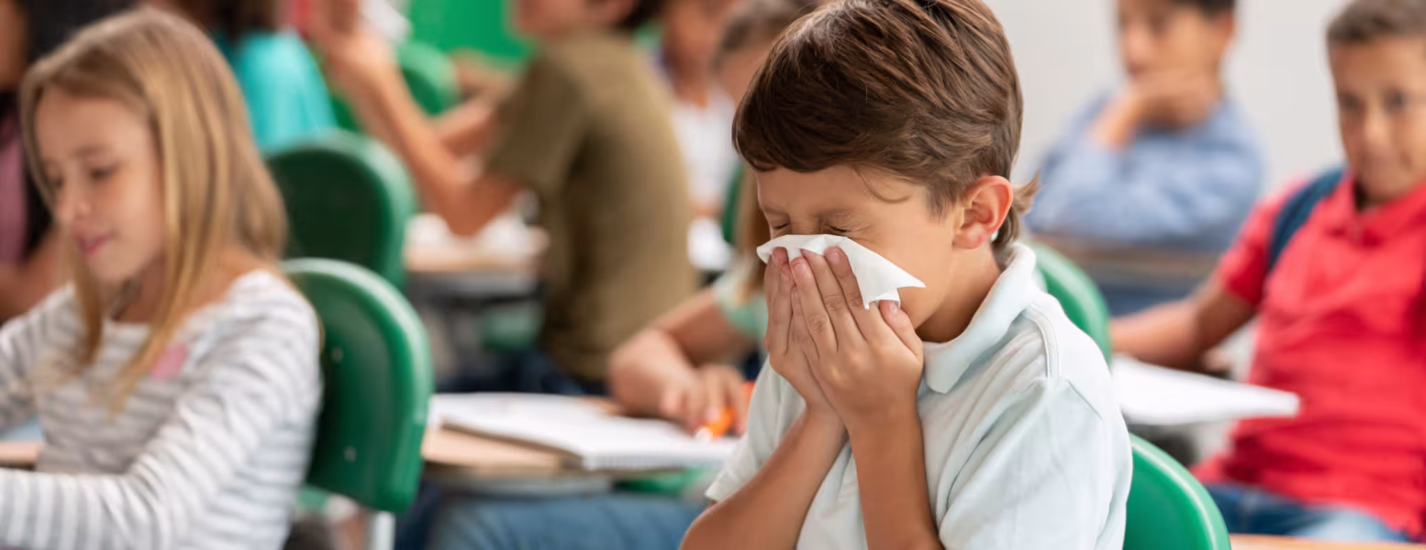Sick boy at the school blowing his nose in class