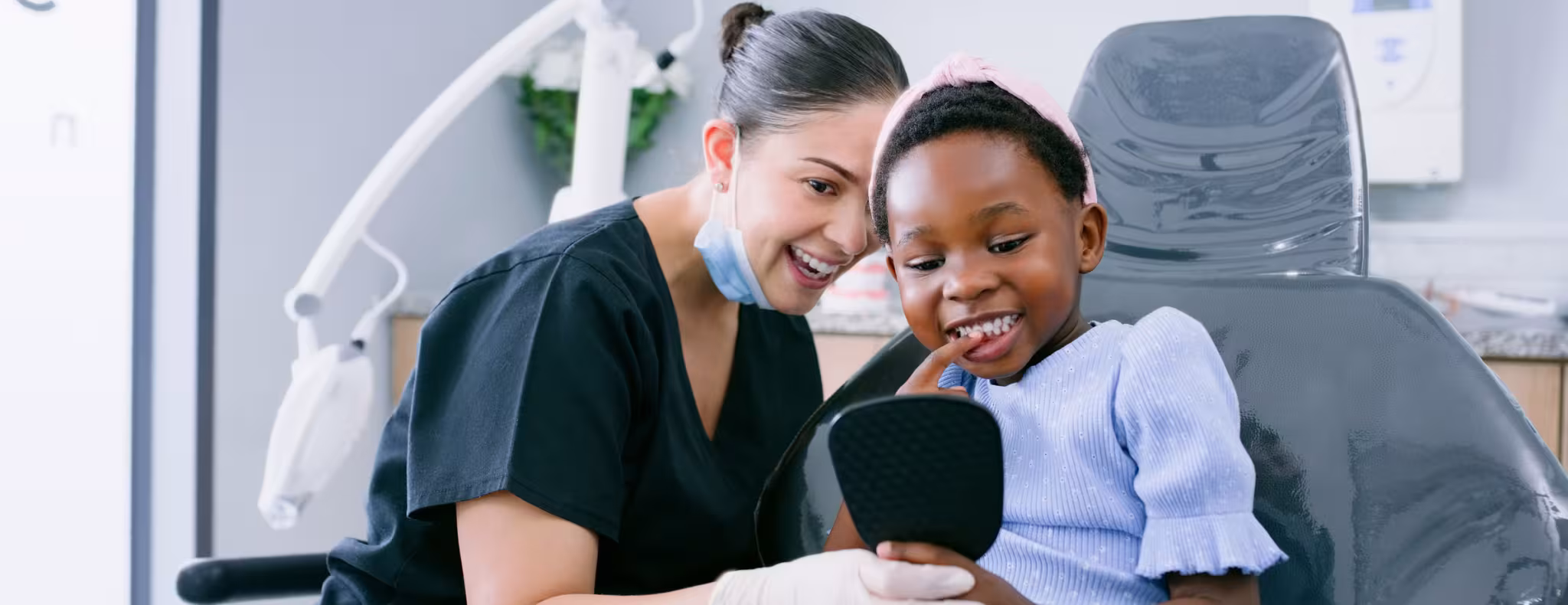 Dentist, child with mirror looking at her teeth while sitting in dental chair