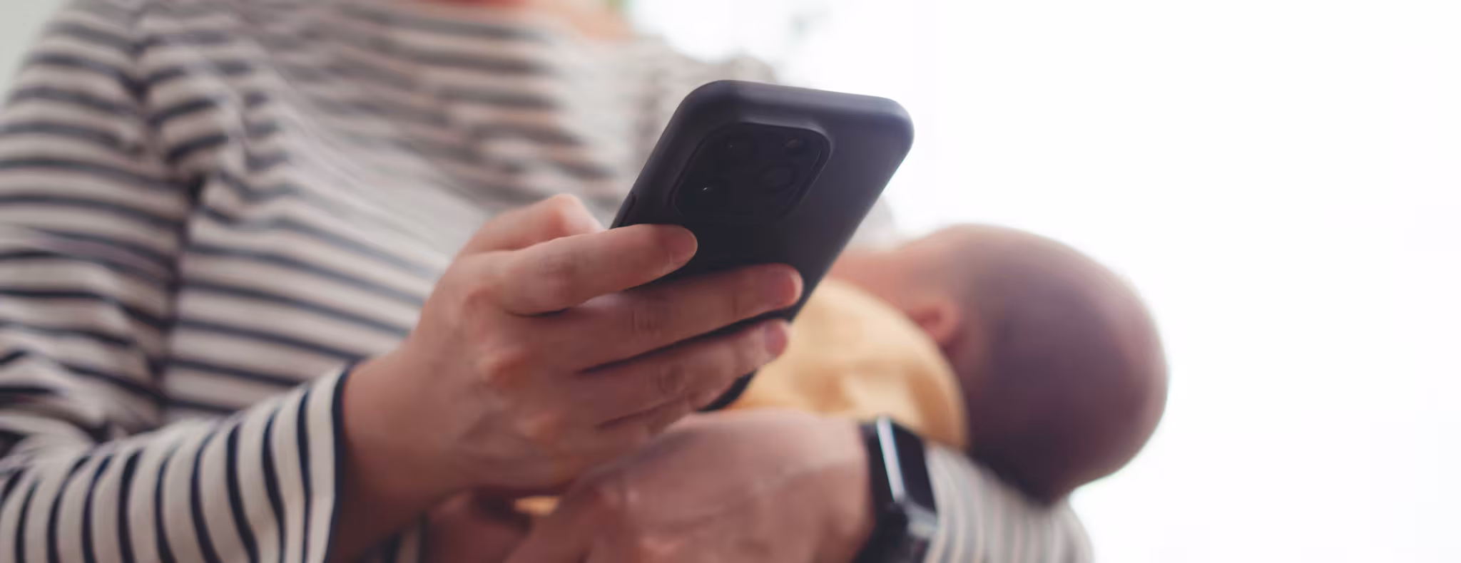 Close up shot of woman carrying her baby and taking a break using smartphone. 