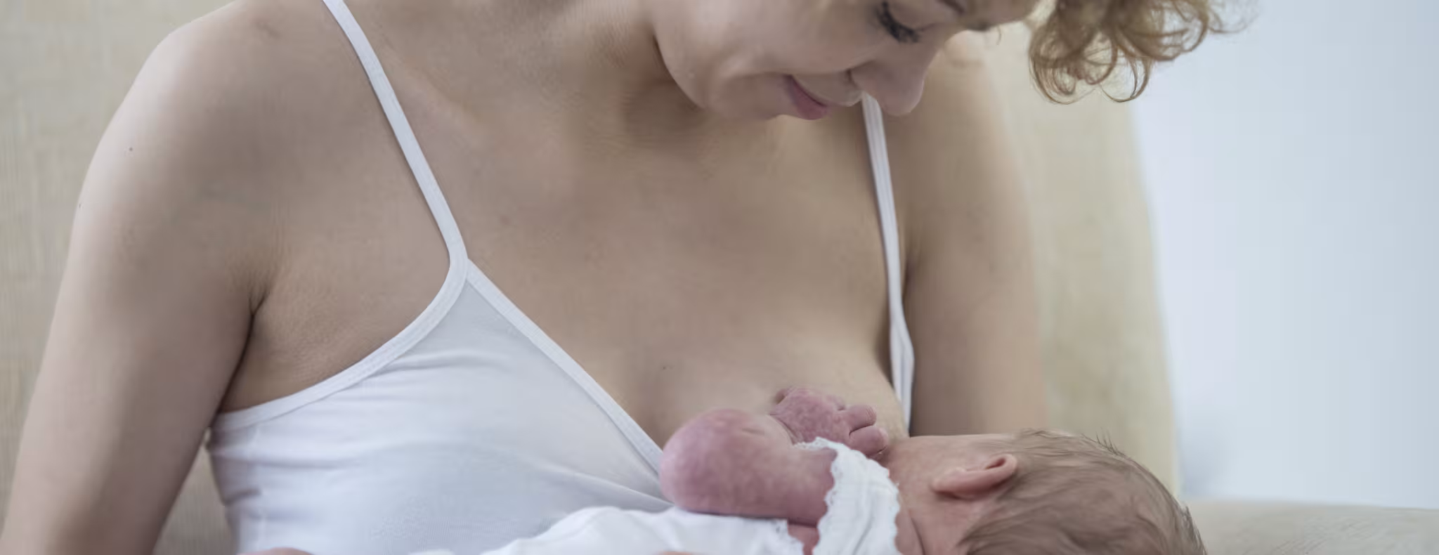 A young adult mother is breastfeeding her newborn baby.