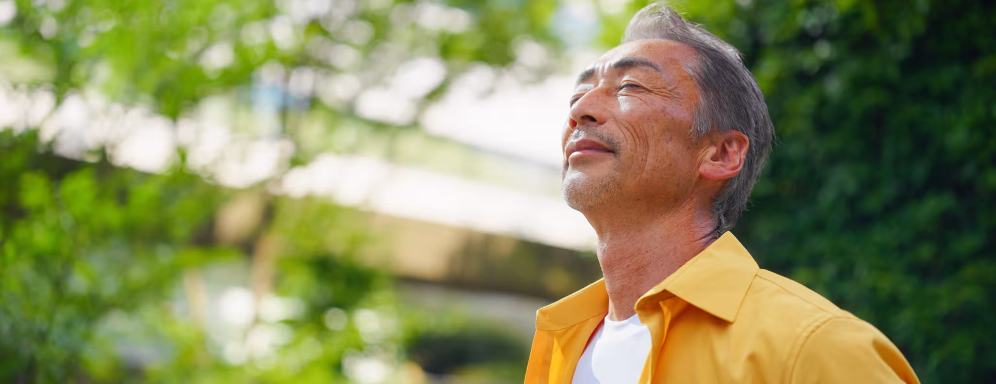 A senior adult man is relaxing in the sun with his eyes closed in the city.