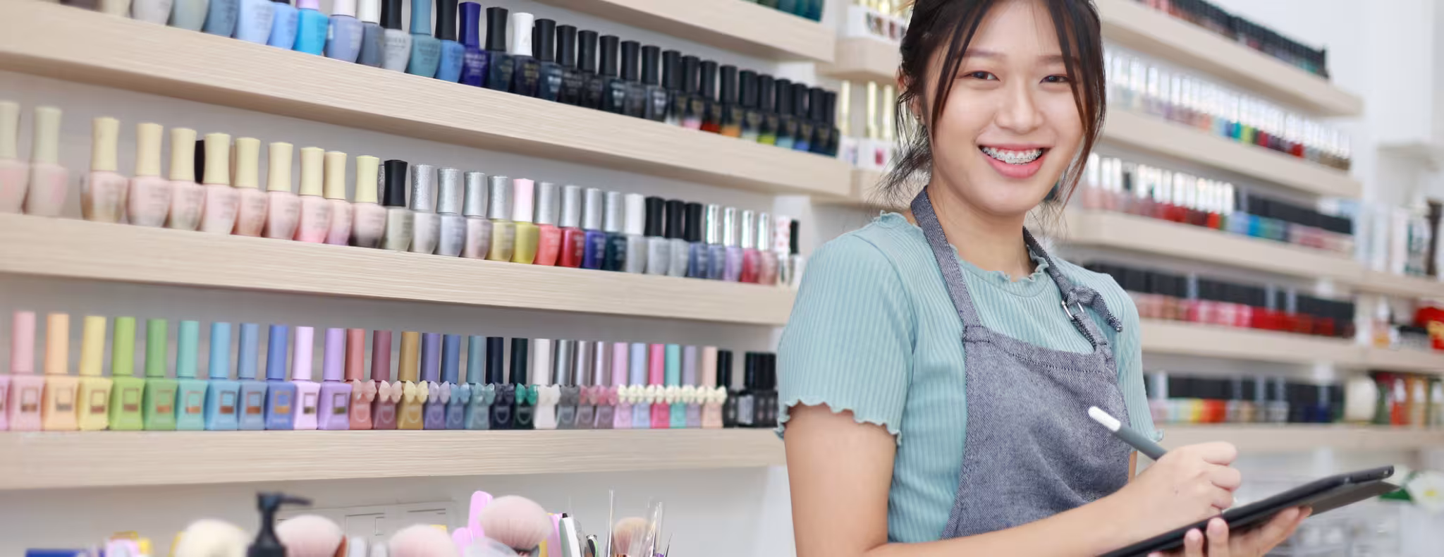 A portrait of a cheerful and confident young Asian female small business owner holding a digital tablet, standing at her nail salon