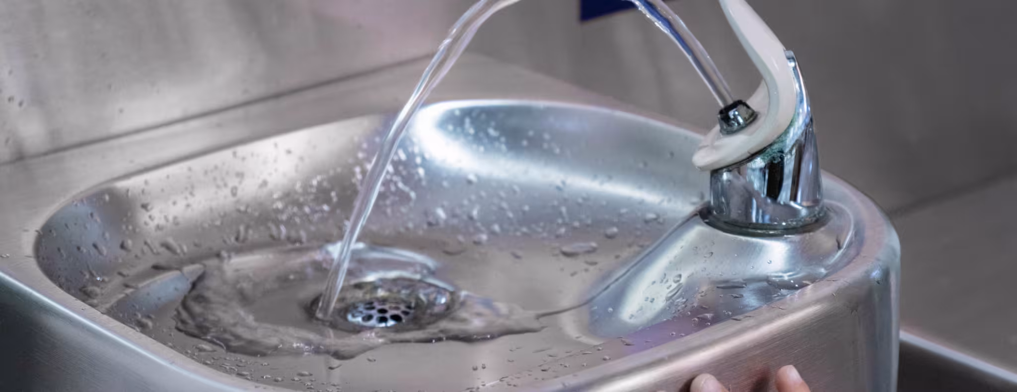 A child touches the handle of a modern drinking fountain as water flows in an indoor setting