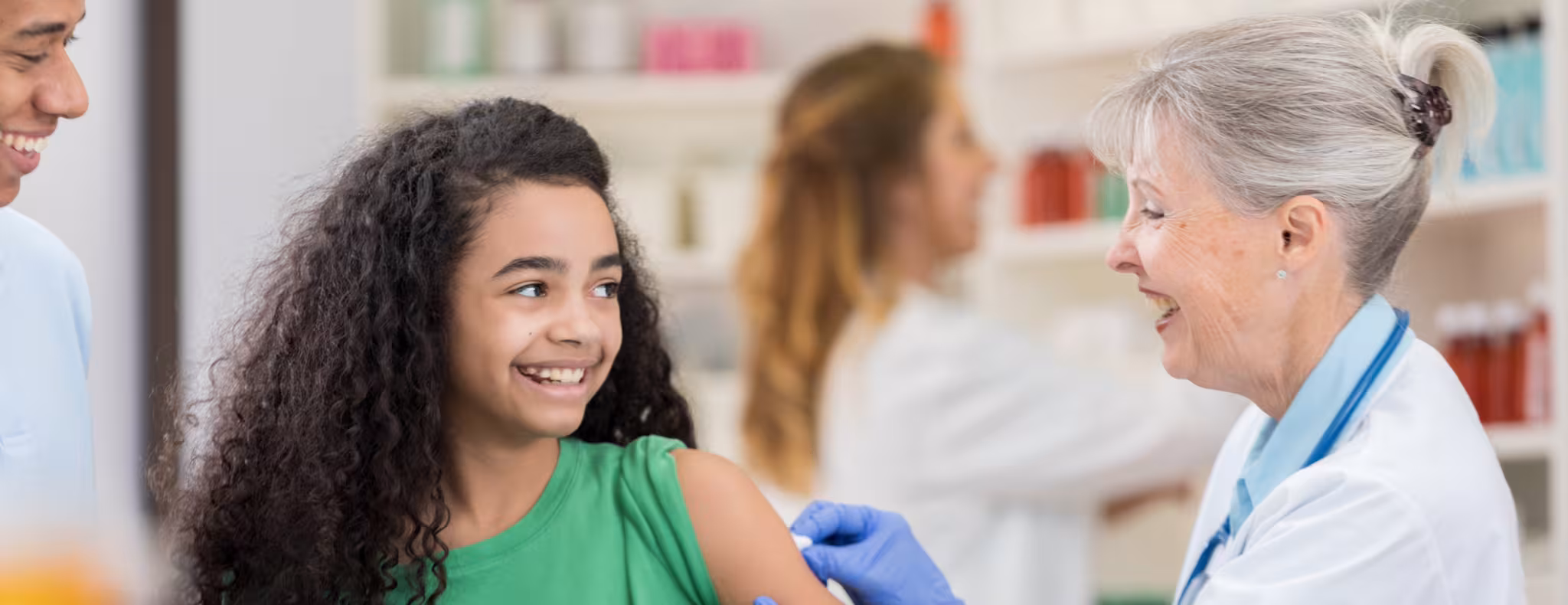 A doctor gives a vaccine injection to a happy, young girl in a bright, indoor clinic setting.