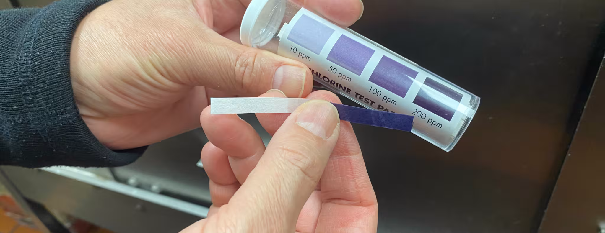 Two hands holding a container of chlorine test strips.