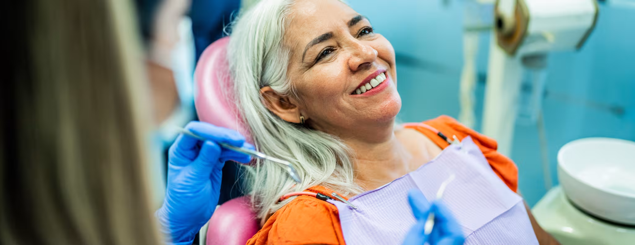 Happy senior woman at dental clinic looking at camera. Her dentist is in the background.