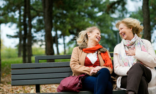 two older women sitting on a park bench laughing